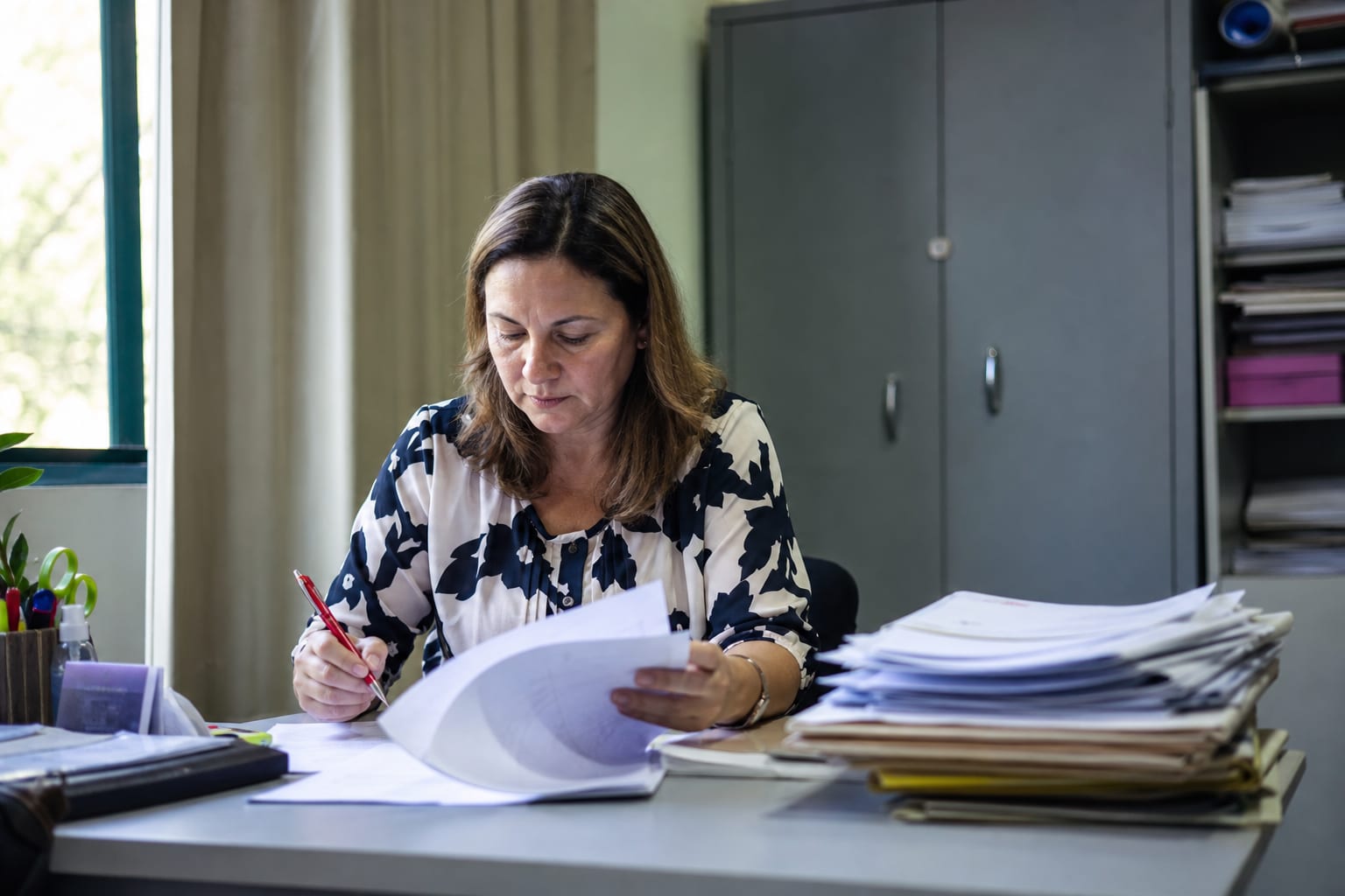 Coordenadora pedagógica revisando planos de aula impressos com caneta na mão